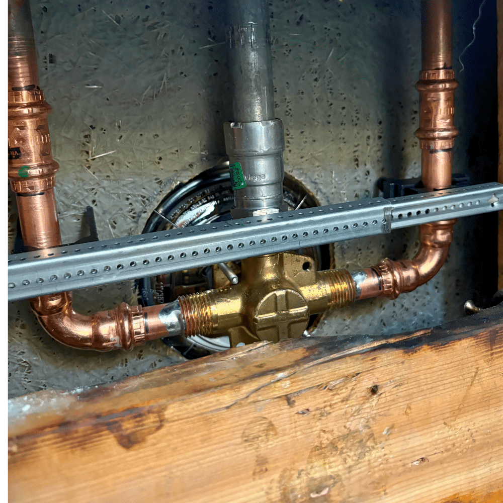 New brass shower valve connected to copper piping inside a Sandy wall